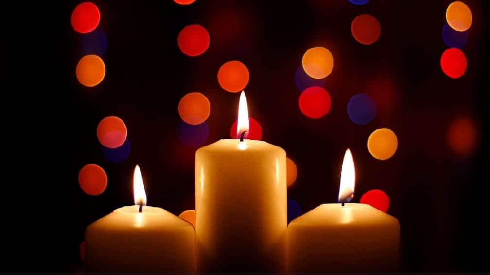 Three burning candles with out of focus decorative lights in the background.